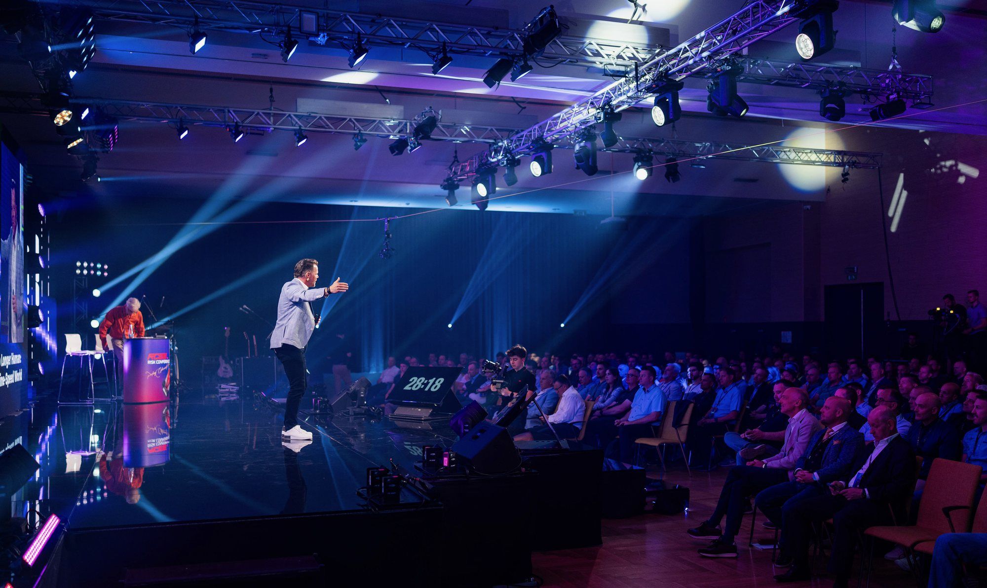 Craig Patterson on stage at RISK Conference 2026, gesturing toward a full audience